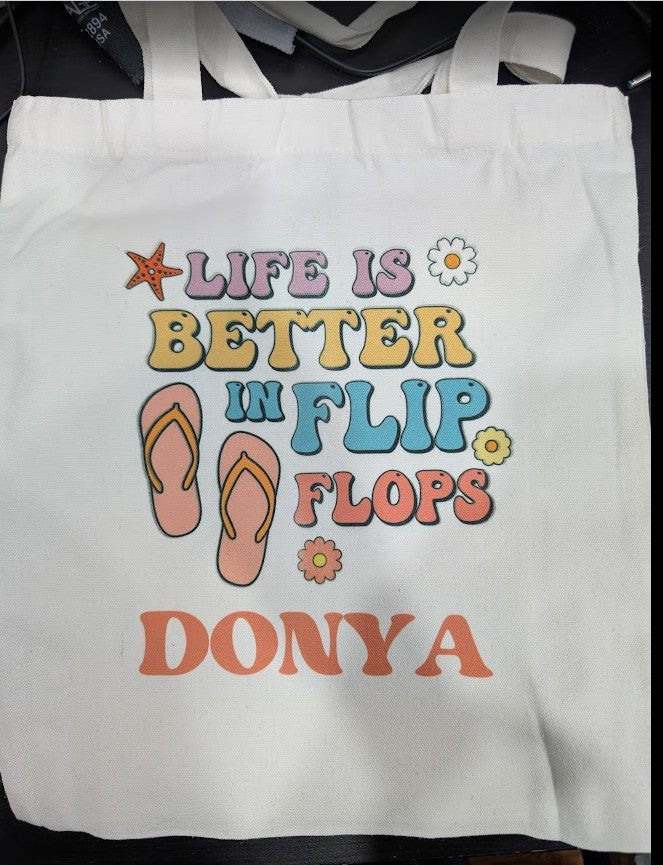White tote bag with colorful text and flip flop design, featuring the brand 'Donya'.